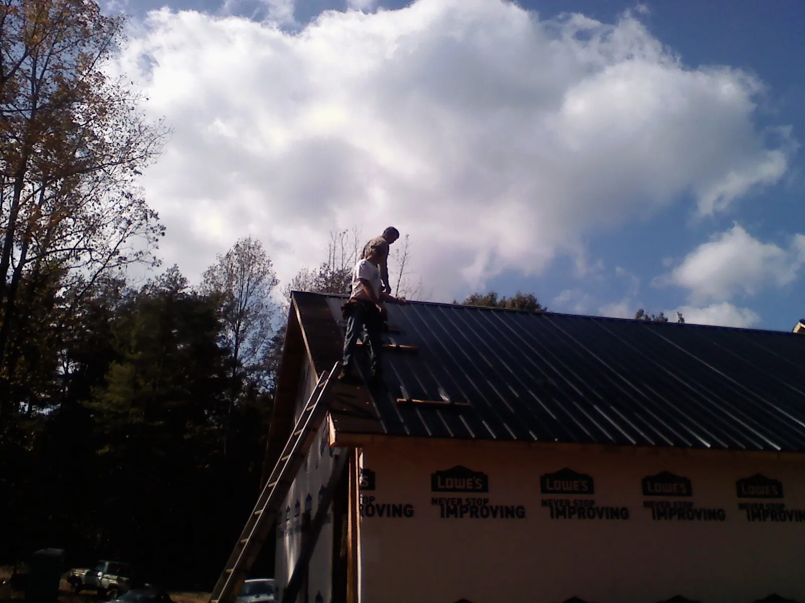 Roofer fastening dark metal panels high against a cloudy sky, from a Roof Inspection job in Montezuma